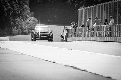 Getarnter schwarzer Hyundai i30 Erlkönig fährt auf einer Rennstrecke, Zuschauer beobachten die Neuvorstellung.